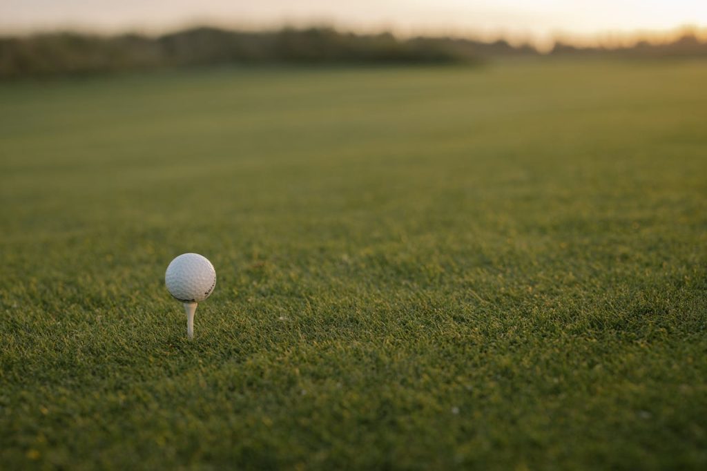 Close-up of a golf ball on tee with green grass and sunset copy space.