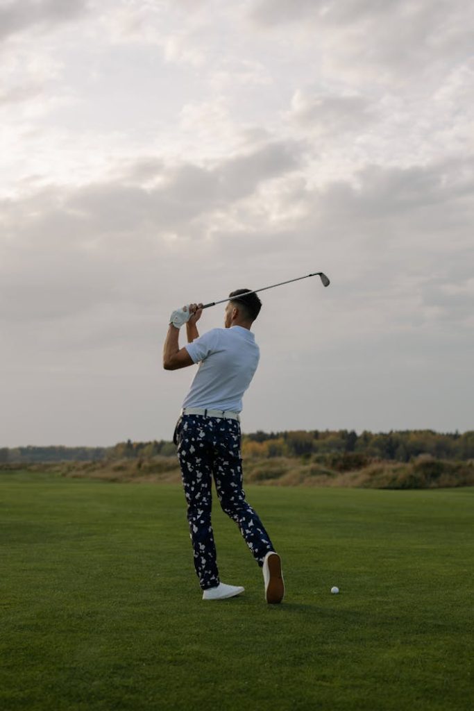 Back view of a man swinging a golf club on a golf course under a cloudy sky.